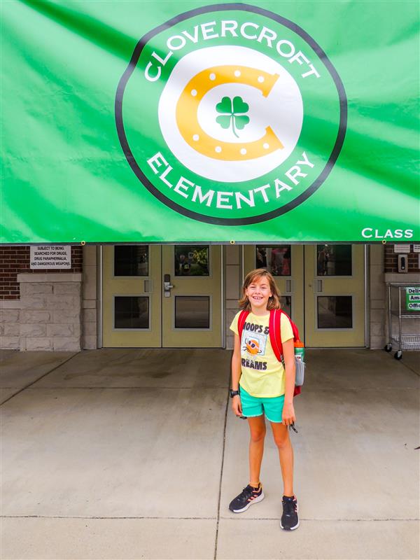 student smiling under the welcome to clovercroft sign